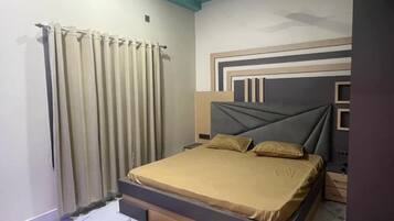 Ein Schlafzimmer mit Bett, Vorhängen, Deckenventilator und einem Kopfteil mit geometrischen Mustern.