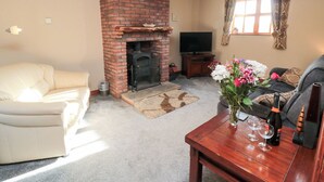 A living room with a brick fireplace, a beige sofa, a wooden coffee table with wine glasses, and a television against the wall. - Beck View (Whitby)
