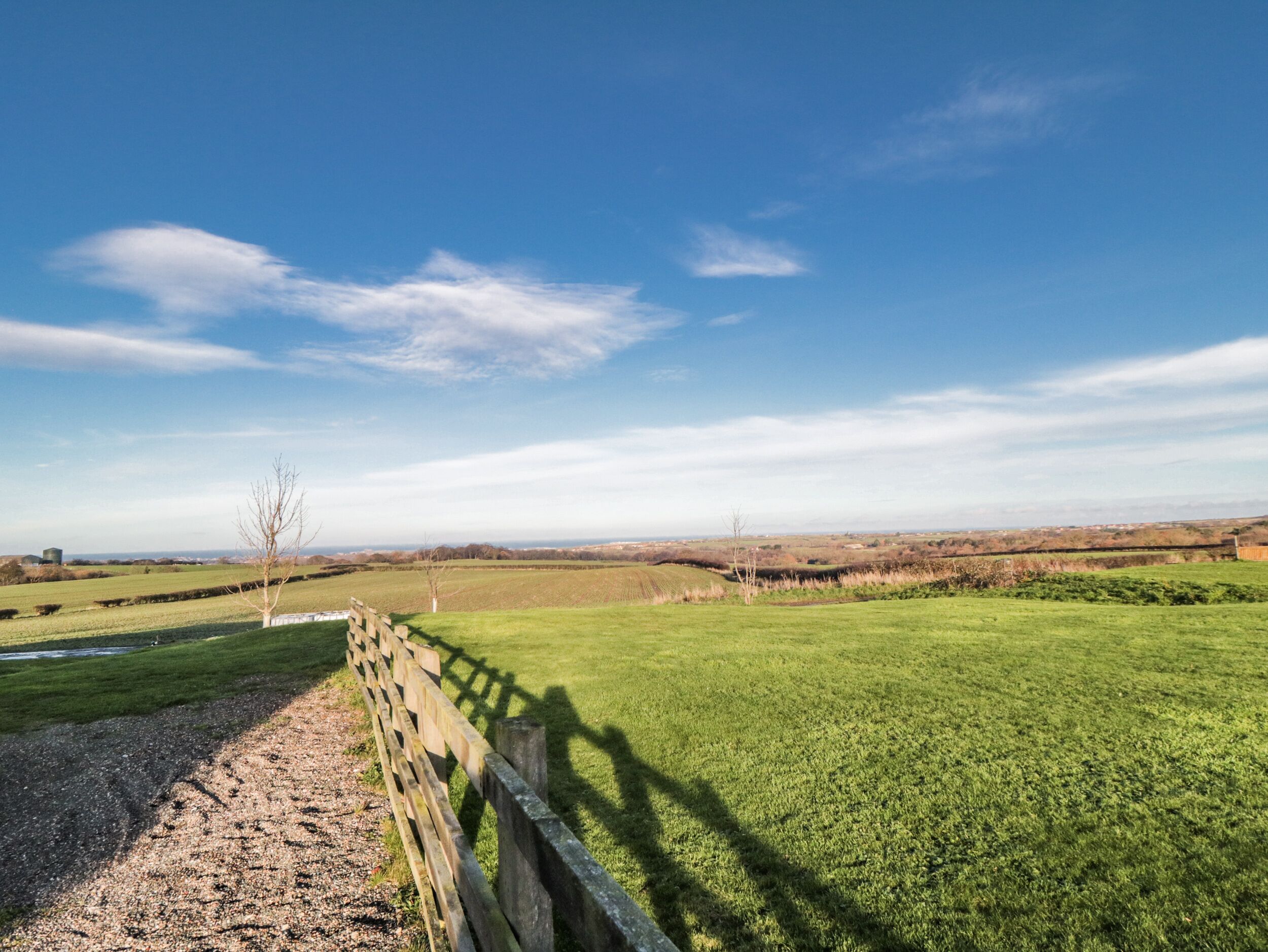 A rural landscape with a wooden fence, open fields, and a clear blue sky.