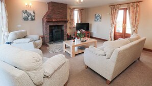 A living room with a brick fireplace, two sofas, a coffee table, and a television. - Pasture View (Whitby)