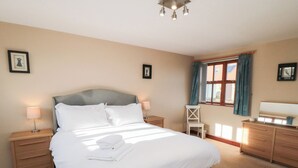 A neatly made bed with white linens, a bedside table with a lamp, a chair, and a dresser with a mirror. - Pasture View (Whitby)