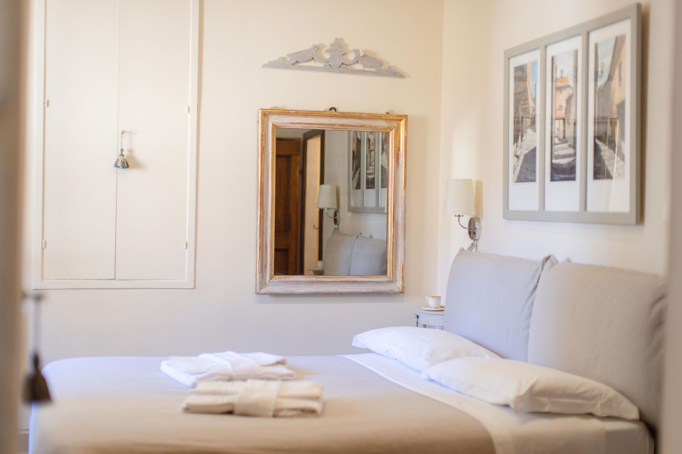A hotel room with a bed, a bedside table with a lamp, a mirror, and a framed picture on the wall.