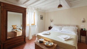 Quarto com um espelho grande, cama com roupa de cama branca, mesa de cabeceira com abajur e cesta de vime com objetos no chão.