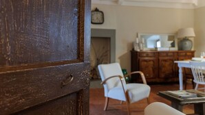 Uma porta de madeira que dá para um quarto com uma cadeira branca, uma mesa e um armário.
