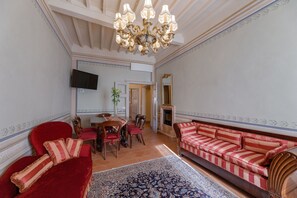 En rummelig stue med en rød sofa, en stribet sofa, en lysekrone, et fjernsyn og en pejs.