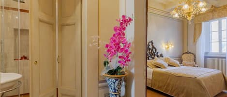 A hotel room with a bathroom, a bed, and a vase with flowers.