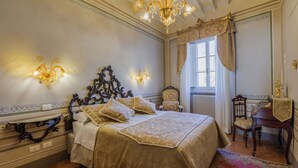 Ein klassisches Schlafzimmer mit einem großen Bett, verzierten Wandleuchtern und einer Chandelier.