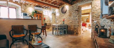 A rustic interior with stone walls, wooden beams, a dining area, and a kitchen with a microwave.
