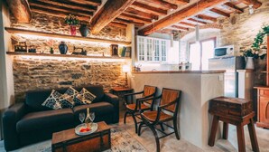 Un'area giorno rustica con parete in pietra, travi in legno al soffitto, un divano con cuscini decorati e un tavolino da caffè con frutta e un bicchiere.