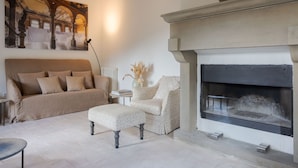 A living room with a fireplace, a sofa, an ottoman, and a painting on the wall. - Tenuta Pomona (Cortona)