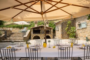 An outdoor dining area with stone walls, a stone staircase, and a rustic stone building with chimneys. - Tenuta Pomona (Cortona)