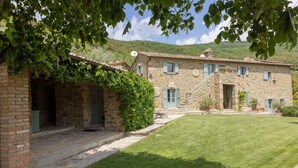 A stone building with a grassy lawn and a hill in the background. - Tenuta Pomona (Cortona)