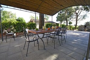 Eine Terrassengruppe mit Tisch und Stühlen, umgeben von Blumentöpfen und Bäumen.