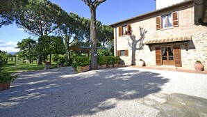 A stone building with a gravel driveway, a tree, and a covered area. - Casa i Pini (Cortona)