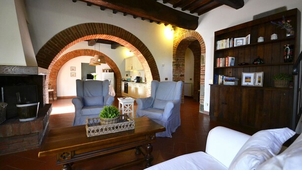 A living room with a fireplace, two armchairs, a coffee table, and a bookshelf. - Casa i Pini (Cortona)