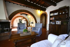 A living room with a fireplace, two armchairs, a coffee table, and a bookshelf. - Casa i Pini (Cortona)