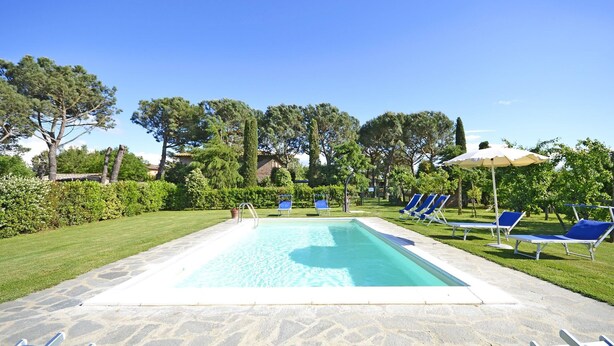 A rectangular swimming pool with a stone deck, surrounded by blue lounge chairs and a few umbrellas. - Casa i Pini (Cortona)