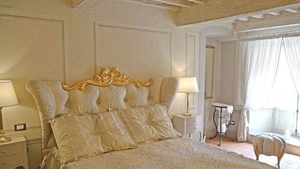 Une chambre à coucher avec un grand lit, deux tables de chevet, une commode, un miroir et une fenêtre avec des rideaux.