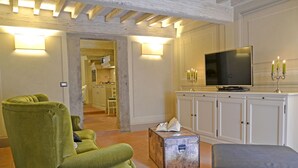 Un salon avec un fauteuil vert, un pouf bleu, un téléviseur et un meuble sur lequel est posé un chandelier.
