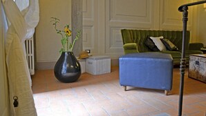 Une pièce avec un canapé vert, un pouf bleu, un vase noir orné de fleurs et un radiateur.