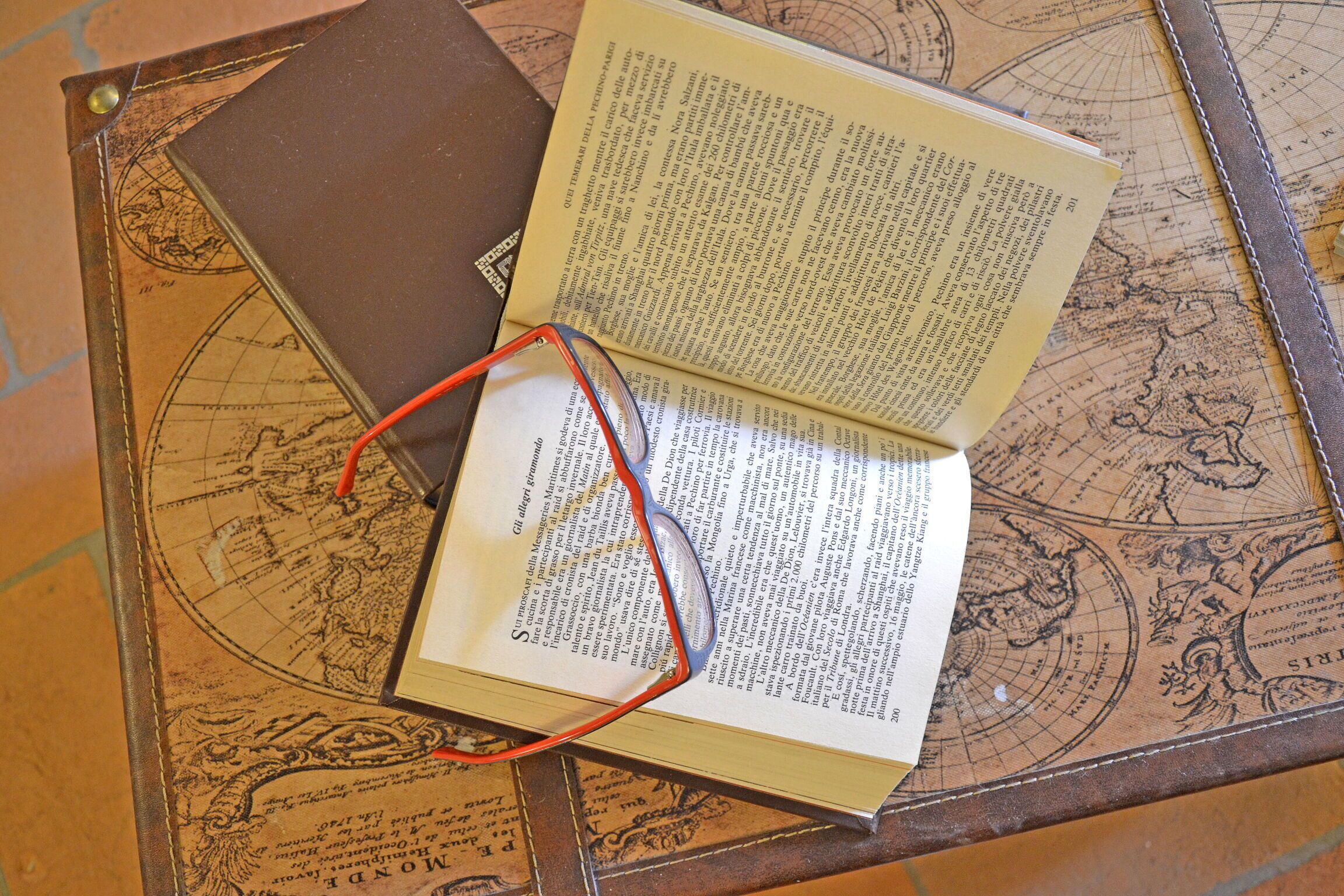 An open book with a bookmark and glasses on a table with a world map design.