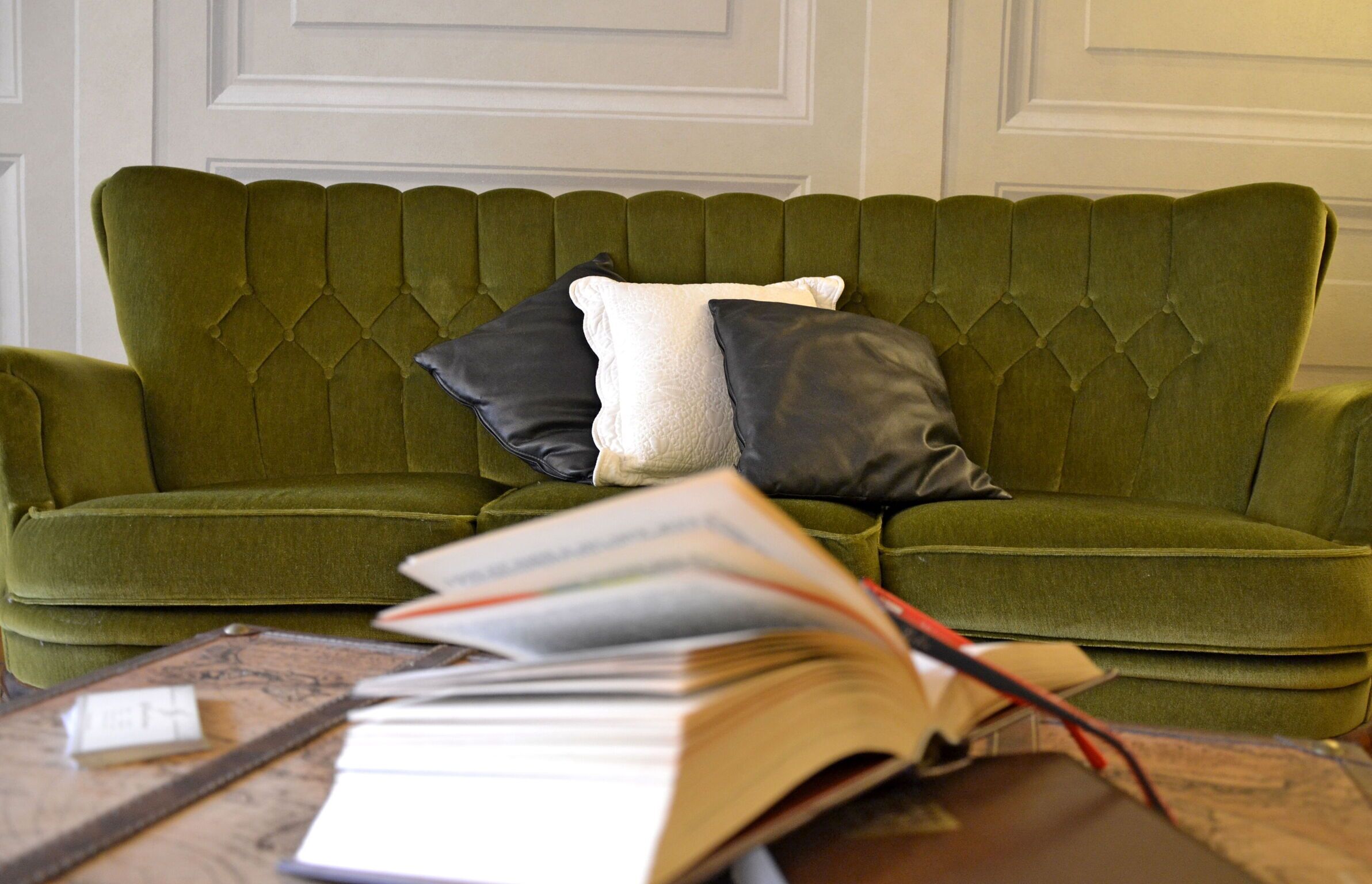 Ein grünes, gepolstertes Sofa mit einer gesteppten Rückenlehne und zwei Kissen, eines weiß und eines schwarz, in einem Raum mit weiß gefälzten Wänden.