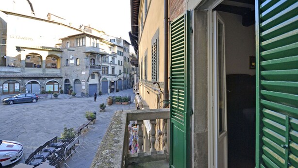 A narrow street with buildings, a balcony with green shutters, and parked cars. - Appartamento La Piazzetta (Cortona)