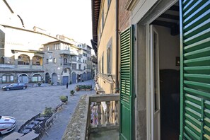 A narrow street with buildings, a balcony with green shutters, and parked cars. - Appartamento La Piazzetta (Cortona)