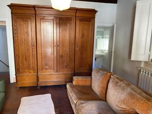 A room with a wooden wardrobe, a sofa, and a small table. - Appartamento La Piazzetta (Cortona)
