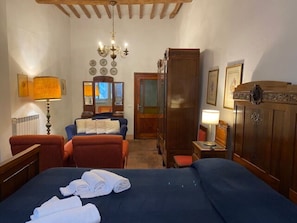 A hotel room with a large bed, two chairs, a wooden wardrobe, a mirror, and a chandelier. - Appartamento La Piazzetta (Cortona)