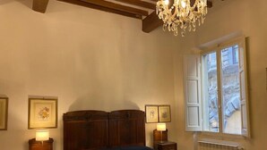 A bedroom with a bed, wooden headboard, bedside tables with lamps, a chandelier, and a window with shutters. - Appartamento La Piazzetta (Cortona)