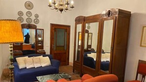 A living room with a sofa, armchairs, a coffee table, a wooden cabinet with mirrors, a chandelier, and wall decorations. - Appartamento La Piazzetta (Cortona)