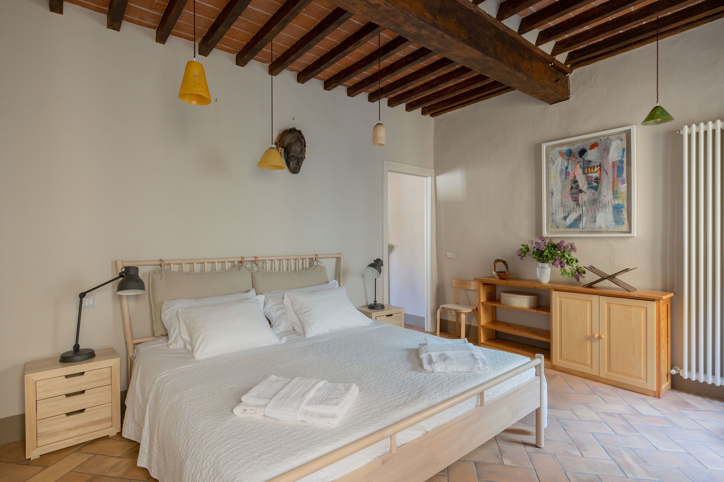 Ein Schlafzimmer mit einem hölzernen Bett, Nachttischen, einem Nachtschränkchen, einem Holzschrank und einem Gemälde an der Wand.