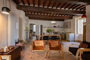 A spacious living area with a wooden ceiling, a dining table with chairs, and a kitchen in the background. - Appartamento Palei (Cortona)