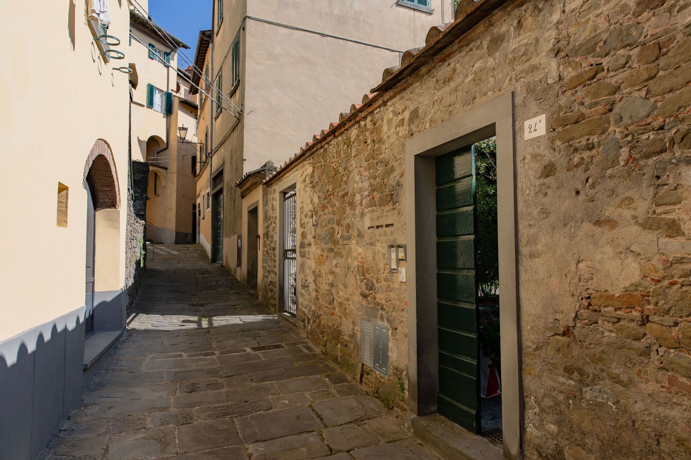 A narrow stone-paved alleyway between buildings with a door marked '24' and a window with shutters.