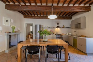 A kitchen with a wooden table, chairs, a vase with flowers, a stove, and a dishwasher. - Appartamento Palei (Cortona)