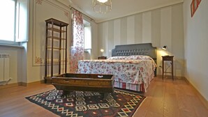 Ein Schlafzimmer mit Bett, Nachttisch, Lampe, Holzkiste und Teppich mit Muster.