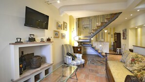 Ein Wohnzimmer mit Fernseher, Kamin, einem gestreiften Sessel, einer Couch und einer Treppe.