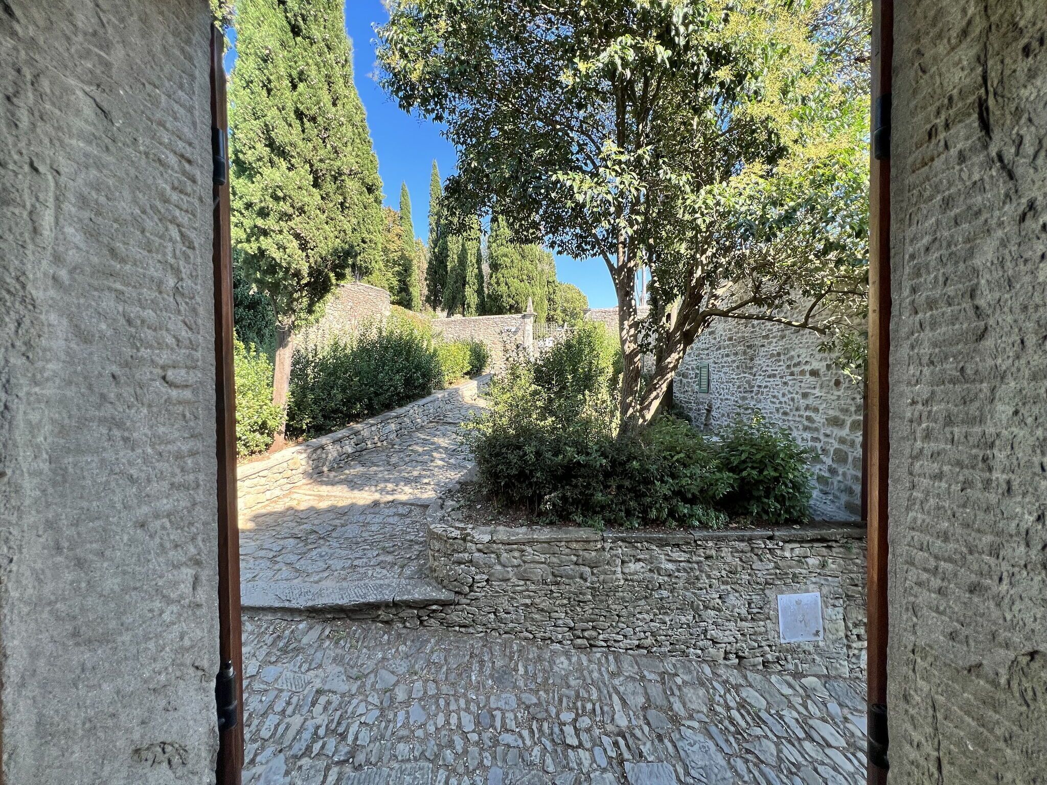 Un chemin de pierres qui traverse un jardin bordé de murs en pierre et d’arbres.
