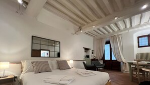 A bedroom with a large bed, a desk, a chair, a mirror, and a window with curtains. - Vicolo Della Scala Rooms - Il Sole (Cortona)