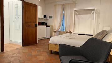 Ein Schlafzimmer mit Bett, Stuhl, Kleiderschrank, Duschbereich und einer kleinen Küchenzeile.