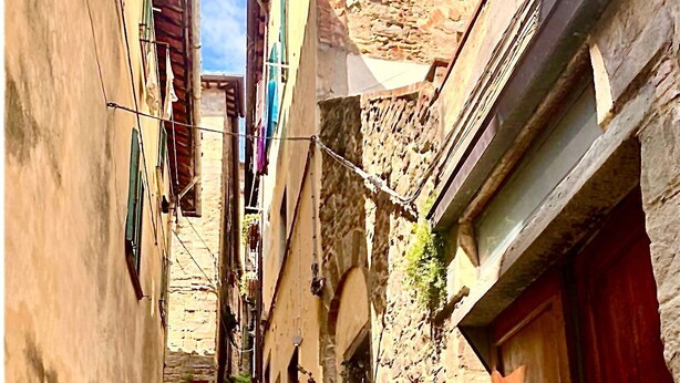 A narrow stone staircase leading up a hillside, flanked by buildings with wooden doors and windows, and hanging laundry. - Vicolo Della Scala Rooms - Il Sole (Cortona)