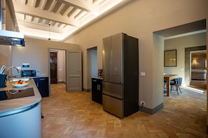 Una cucina moderna con un frigorifero grande, un forno a microonde e un lavello. Si intravede sullo sfondo una zona pranzo con tavolo e sedie.