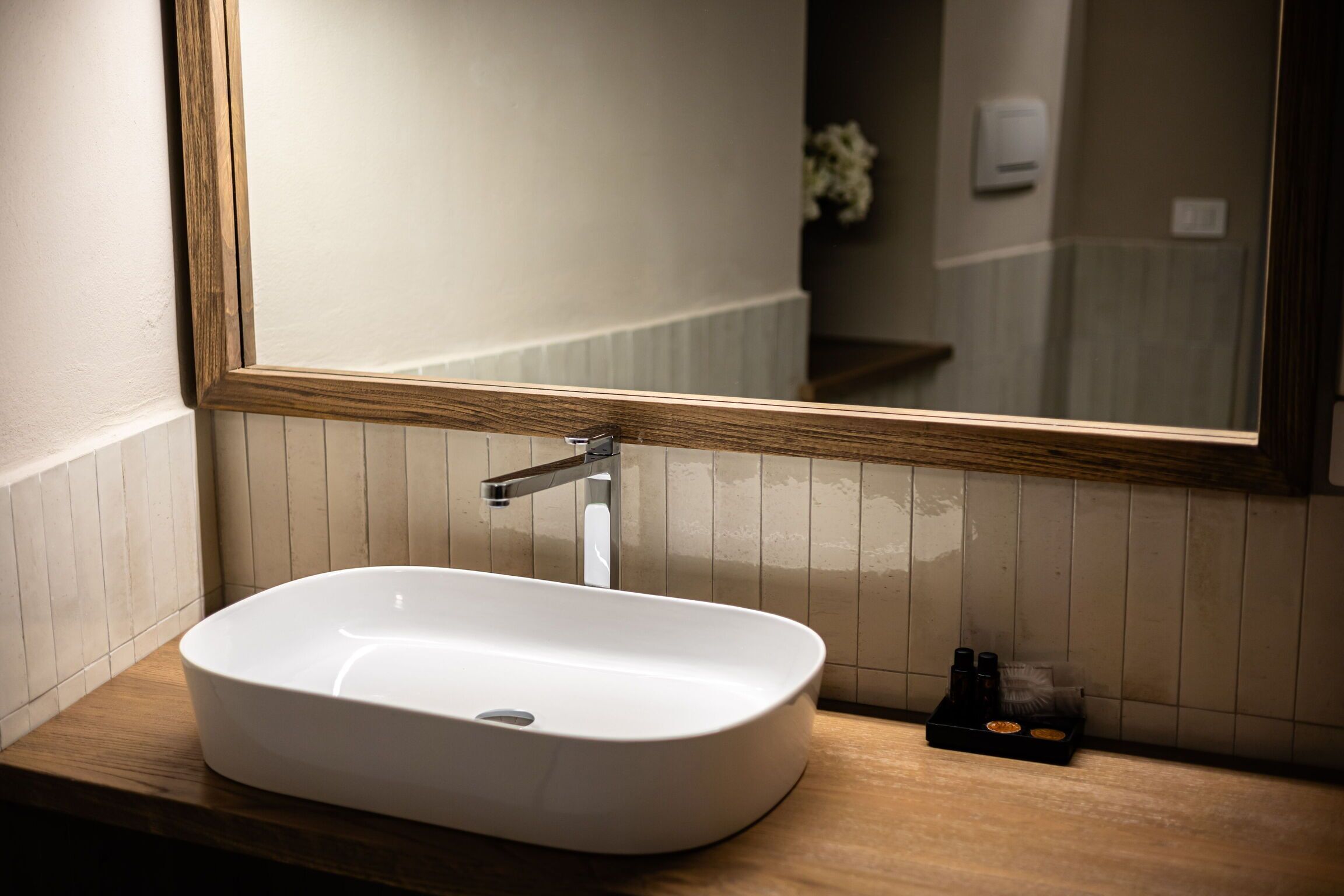 A bathroom with a white sink, wooden countertop, and a mirror with a wooden frame.