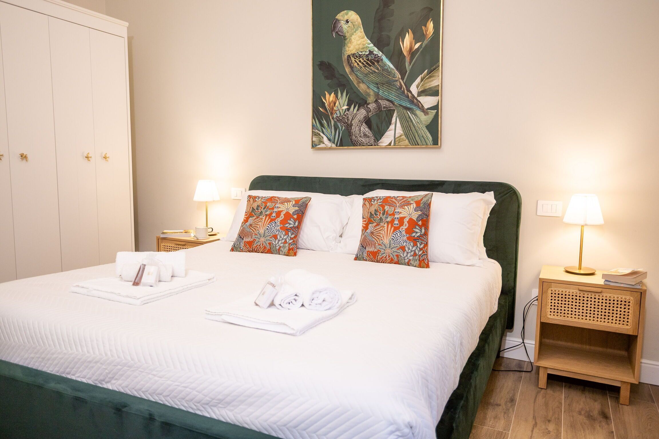 A neatly made bed with pillows, a wall-mounted painting of a bird, and bedside lamps.