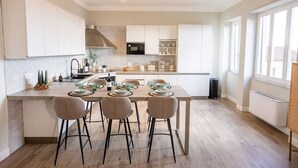 Una cucina moderna con mobili bianchi, un'isola centrale con sgabelli da bar e un tavolo da pranzo per quattro persone.