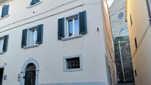 A building with a beige facade, multiple windows with shutters, and a stone staircase leading to a lower level. - Casa Del Borgo (Cortona)