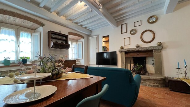 A cozy living room with a fireplace, a television, and a dining area with a table and chairs. - Casa Del Borgo (Cortona)