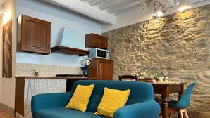 A cozy living area with a blue sofa, yellow cushions, a wooden dining table, and a stone wall. - Casa Del Borgo (Cortona)