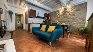 A spacious living area with a teal sofa, a stone wall, and a kitchen in the background. - Casa Del Borgo (Cortona)